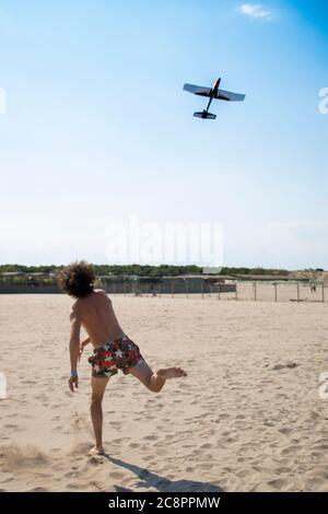 Jeune homme, portant un maillot de bain, jetant un avion ou un planeur sur la plage en été. Arrière-plan ou fond d'écran avec espace de copie. Tir vertical. Rosolina Banque D'Images