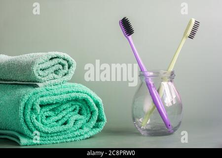 deux brosses à dents dans un pot en verre et deux serviettes en bleu-vert sur fond gris Banque D'Images