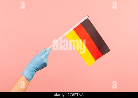 Profil vue latérale gros plan de la main humaine en gants chirurgicaux bleus tenant le drapeau allemand. Jour d'Allemagne - 3 octobre. En intérieur, prise de vue en studio, isolé sur p Banque D'Images