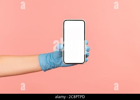 Vue latérale du profil gros plan de la main humaine avec des gants chirurgicaux bleus tenant et montrant un smartphone écran vertical vide. Intérieur, studio, isolé Banque D'Images