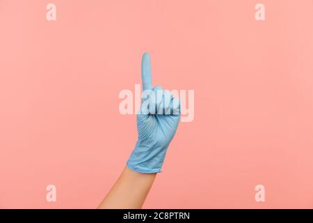 Vue latérale du profil gros plan de la main humaine avec des gants chirurgicaux bleus montrant le numéro un avec le doigt ou montrant le côté. Vue en intérieur, prise en studio, isolée sur pi Banque D'Images