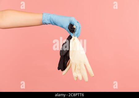 Vue latérale du profil gros plan de la main humaine avec des gants chirurgicaux bleus tenant des gants blancs et noirs. Vue en intérieur, prise de vue en studio, isolée sur fond rose. Banque D'Images