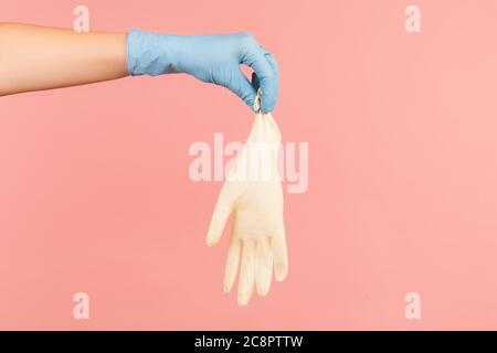 Vue latérale du profil gros plan de la main humaine avec des gants chirurgicaux bleus tenant des gants blancs. Vue en studio, isolée sur fond rose. Banque D'Images