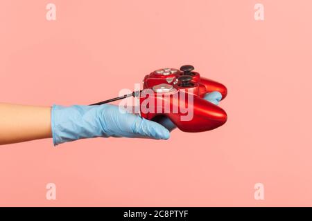 Vue latérale du profil gros plan de la main humaine en gants chirurgicaux bleus tenant la manette de jeu rouge. Prise de vue en studio, à l'intérieur, isolée sur fond rose. Banque D'Images