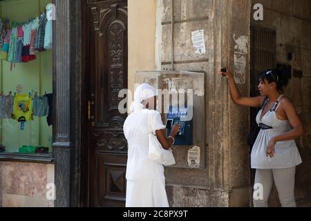 La Havane / Cuba - 04.15.2015: Jeune femme cubaine portant une robe blanche Santeria faisant un appel téléphonique sur un téléphone public Banque D'Images