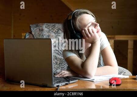 Une jeune fille d'école fatiguée regarde la fenêtre pendant un webinaire d'école en ligne. Le concept de la charge de travail excessive des élèves à l'école Banque D'Images