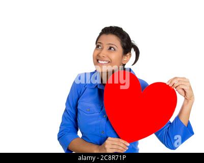 Gros plan portrait de la jolie femme souriante tenant le cœur rouge à la poitrine rêvant, dans l'amour, isolée sur fond blanc. Émotion positive du visage Banque D'Images