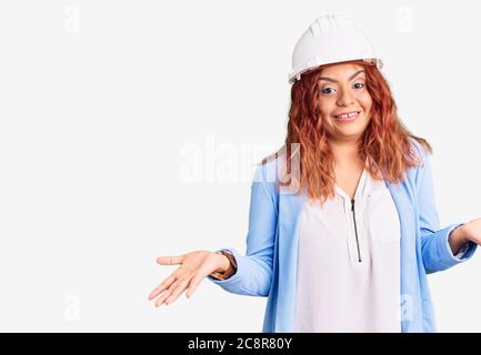 Jeune femme latine portant un architecte hardhat expression sans indice et confuse avec les bras et les mains soulevées. Doute concept. Banque D'Images