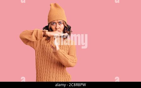 Jeune femme de race mixte, portant un pull en laine et un chapeau d'hiver, faisant un geste de temps avec les mains, frustré et sérieux visage Banque D'Images
