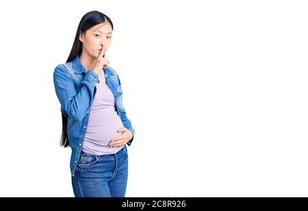 Jeune belle femme chinoise enceinte s'attendant à bébé demandant à être calme avec le doigt sur les lèvres. Silence et secret concept. Banque D'Images