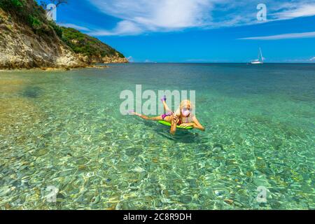 Femme avec le signe de victoire main sur matelas flottant de plage avec un masque chirurgical rose pendant Covid-19. Femme nageant à Prunini o Seccione Beach dans Banque D'Images