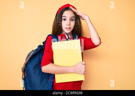 Adorable enfant hispanique fille portant un sac à dos étudiant et un casque tenant livre stressé et frustré avec la main sur la tête, surpris et fâché visage Banque D'Images