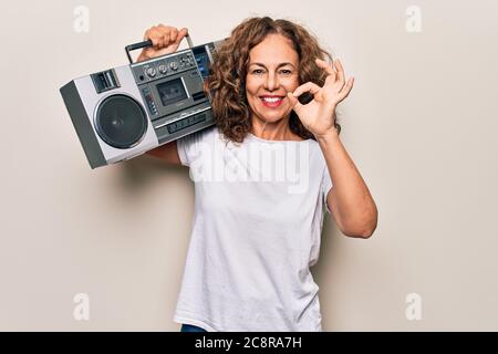 Moyen âge brunette hipster femme tenant la musique rétro boombox sur un fond isolé faire signe ok avec les doigts, souriant sympathique gesting excellent Banque D'Images
