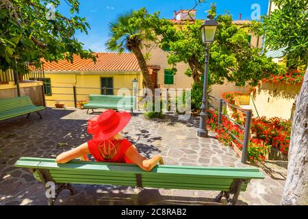 Style de vie femme en rouge assis sur le banc à Marciana Marina, le vieux quartier fleuri Borgo al Cotone. Tourisme sur voyage de vacances en Italie, île d'Elbe Banque D'Images
