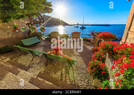 Femme en rouge avec chapeau à Marciana Marina au coucher du soleil, le vieux quartier fleuri Borgo al Cotone: Signifiant VILLAGE DE COTON. Tourisme en vacances Banque D'Images