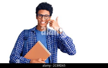 Jeune africain américain portant le sac à dos étudiant tenant le livre pointant du doigt vers le visage et le nez, souriant gai. Concept de beauté Banque D'Images