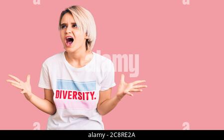 Jeune belle femme blonde portant t shirt avec message de mot de diversité fou et fou criant et hurlant avec l'expression agressive et les bras levés Banque D'Images