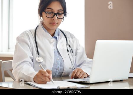 Femme indienne médecin remplissant le formulaire médical travaillant avec un ordinateur portable sur le lieu de travail. Banque D'Images