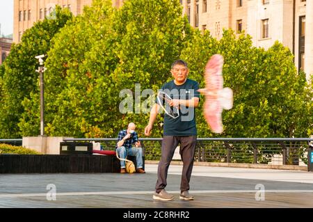 Un retraité vole un cerf-volant en forme d'oiseau sur la promenade Bund de Shanghai en début de matinée. Banque D'Images