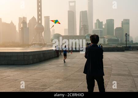 Un homme volant un cerf-volant tôt le matin sur le Bund de Shanghai avec la ligne d'horizon de Pudong en arrière-plan. Banque D'Images