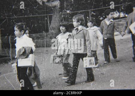 Fin 70s vintage noir et blanc de style de vie photographie d'un groupe d'enfants d'école marchant le long du trottoir. Banque D'Images