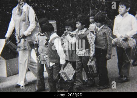 Fin 70s vintage noir et blanc de style de vie photographie d'un groupe d'enfants d'école marchant le long du trottoir. Banque D'Images