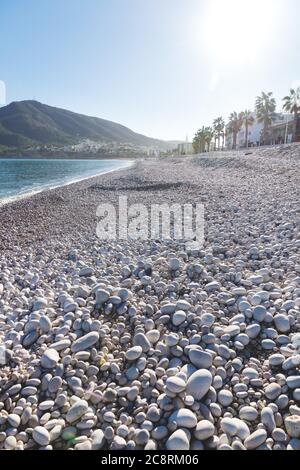 Plage en pierre blanche d'Albir avec vue sur la promenade alignée avec les palmiers et la montagne, Costa Blanca, Espagne Banque D'Images