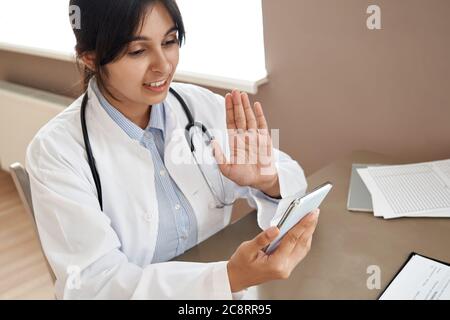 Femme indienne médecin, appel vidéo de patient dans l'application de téléphone mobile en ligne. Banque D'Images