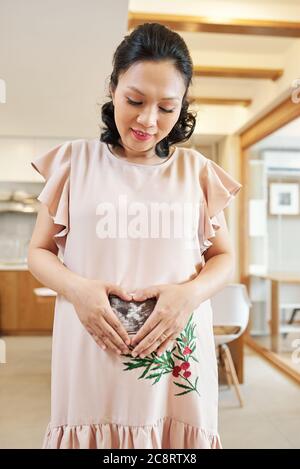 Souriante Jolie Femme Asiatique En Robe Rose Clair Faisant Le Geste De Coeur En Montrant L Echographie De Son Bebe Photo Stock Alamy