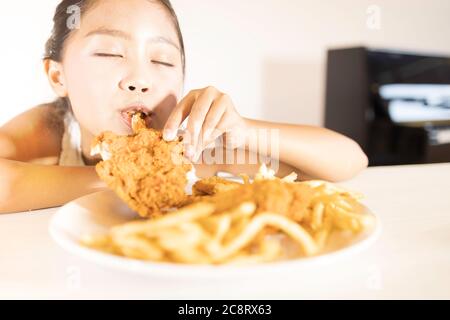 Une adorable fille asiatique apprécie de manger du poulet frit et des frites. Banque D'Images