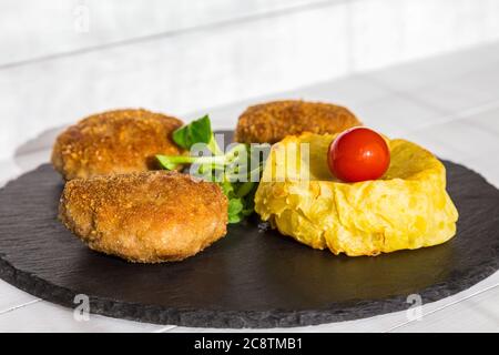 Hamburgers ou côtelettes faits maison avec pommes de terre formées cuites au four et salade sur plaque de pierre et table en bois. Banque D'Images