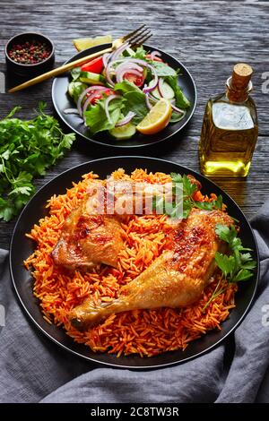 Quartiers de cuisses de poulet croustillants cuits sur du riz à la tomate indienne et salade de tomates fraîches, petits épinards, concombres, laitue, oignon rouge avec citron sur une bla Banque D'Images