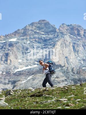 Alpiniste mâle en lunettes de soleil randonnée seule dans la région montagneuse. Randonnée avec sac à dos le long de la piste rocheuse avec montagne Matterhorn sur fond. Concept de voyage, randonnée, alpinisme Banque D'Images