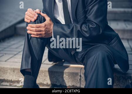 Homme en costume souffrant de douleurs au genou dans la rue Banque D'Images