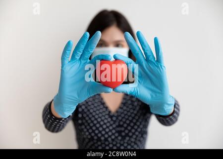 Gros plan de la femme en masque de visage montrer cœur rouge jouet Banque D'Images