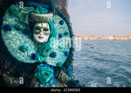 Un beau masque pose devant le canal de Venise dans un costume bleu clair avec une rose. Banque D'Images