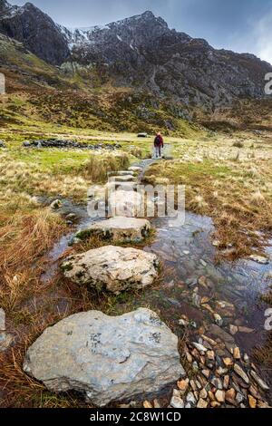 Des pierres qui traversent l'eau de fonte des montagnes enneigées de Glyder Fawr menant à Llyn Idwal, parc national de Snowdonia, au nord du pays de Galles Banque D'Images