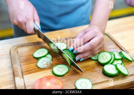 les mains des femelles coupent le concombre en tranches sur une planche à découper en bois Banque D'Images