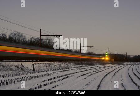 À l'heure bleue, à l'aube d'un hiver froid, un train international passe à Tinglev au Danemark, laissant des sentiers légers pendant la longue période Banque D'Images