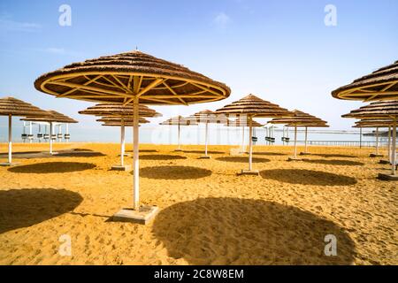 Belle plage avec des chaises de plage et des parasols en chaume dans la ville balnéaire d'Ein Bokek Israël. Banque D'Images