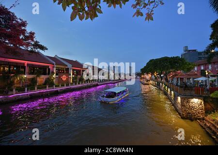 Un bateau à aubes se déplace en amont sur la rivière Malacca au crépuscule avec des lumières vives reflétées dans l'eau. Banque D'Images