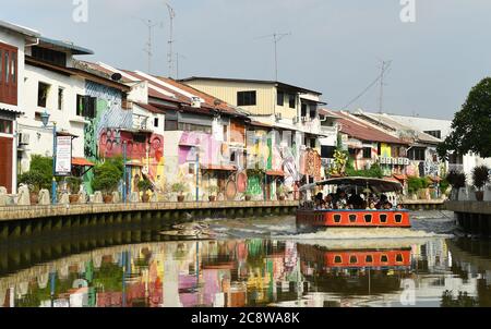 Les écoliers font un mouvement de vague depuis un bateau de tourisme qui descend la rivière Malacca avec de l'art de rue sur les bâtiments au bord de la rivière à Malacca Malaisie. Banque D'Images