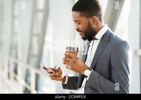 Bon homme d'affaires africain utilisant un téléphone portable ayant un café dans le terminal de l'aéroport Banque D'Images