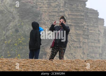 West Bay, Dorset, Royaume-Uni. 27 juillet 2020. Météo Royaume-Uni. Une mère et un fils affronte les conditions non saisonnières sur la plage de la station balnéaire de West Bay à Dorset, le matin de vents violents et de pluie. Crédit photo : Graham Hunt/Alay Live News Banque D'Images