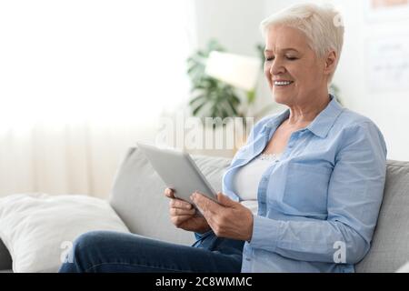Applications pour les aînés. Femme âgée utilisant une tablette numérique tout en se reposant à la maison Banque D'Images