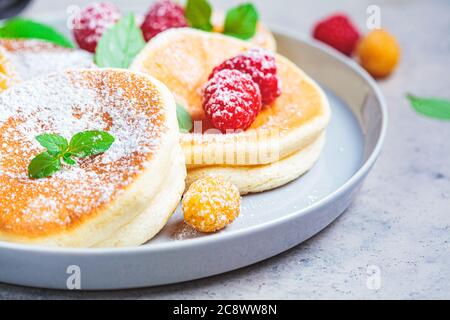 Crêpes japonaises moelleuses aux framboises dans une assiette grise, fond gris. Concept de cuisine japonaise. Banque D'Images