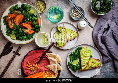 Table de déjeuner végétalienne, vue sur le dessus. Assiette de salade de patate douce cuite au four, toasts d'avocat et houmous sur fond sombre. Banque D'Images