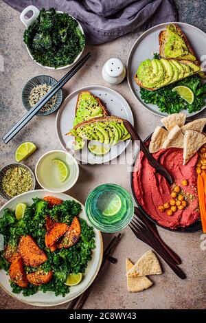 Table de déjeuner végétalienne, vue sur le dessus. Assiette de salade de patate douce cuite au four, toasts d'avocat et houmous sur fond sombre. Banque D'Images