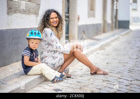 Belle femme assise dans la rue à côté d'un petit garçon avec un casque de vélo Banque D'Images