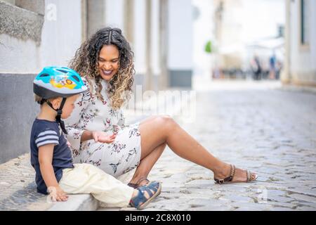 Belle femme assise dans la rue à côté d'un petit garçon avec un casque de vélo Banque D'Images